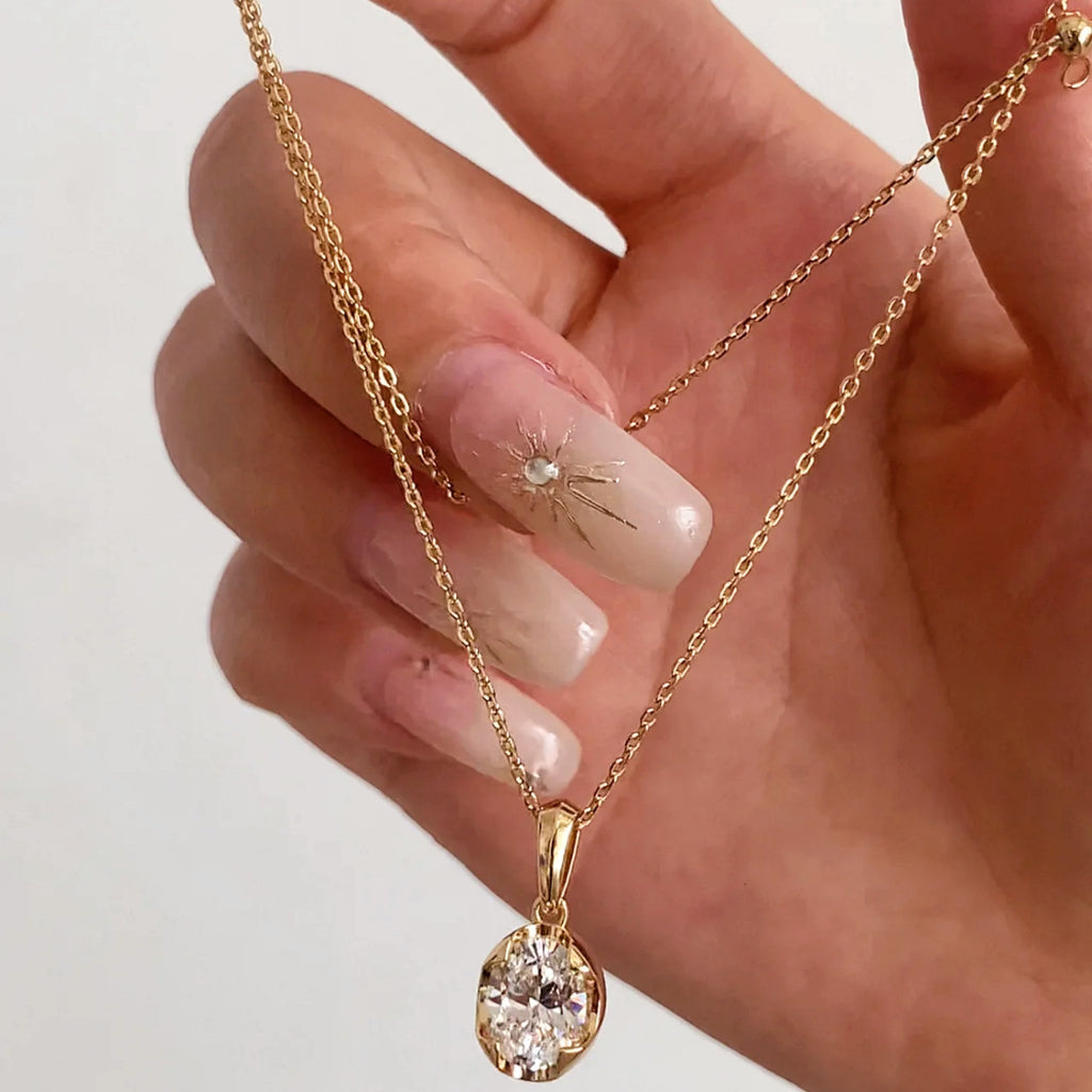 Gold necklace with a teardrop-shaped pendant held by a hand against a light background