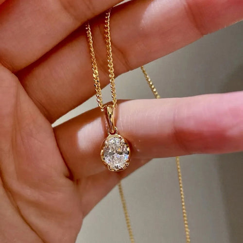 Gold necklace with a diamond pendant held in a hand against a neutral background