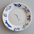 A white ceramic plate with blue line-art illustrations of cats in various poses, shown on a dark wooden table.
