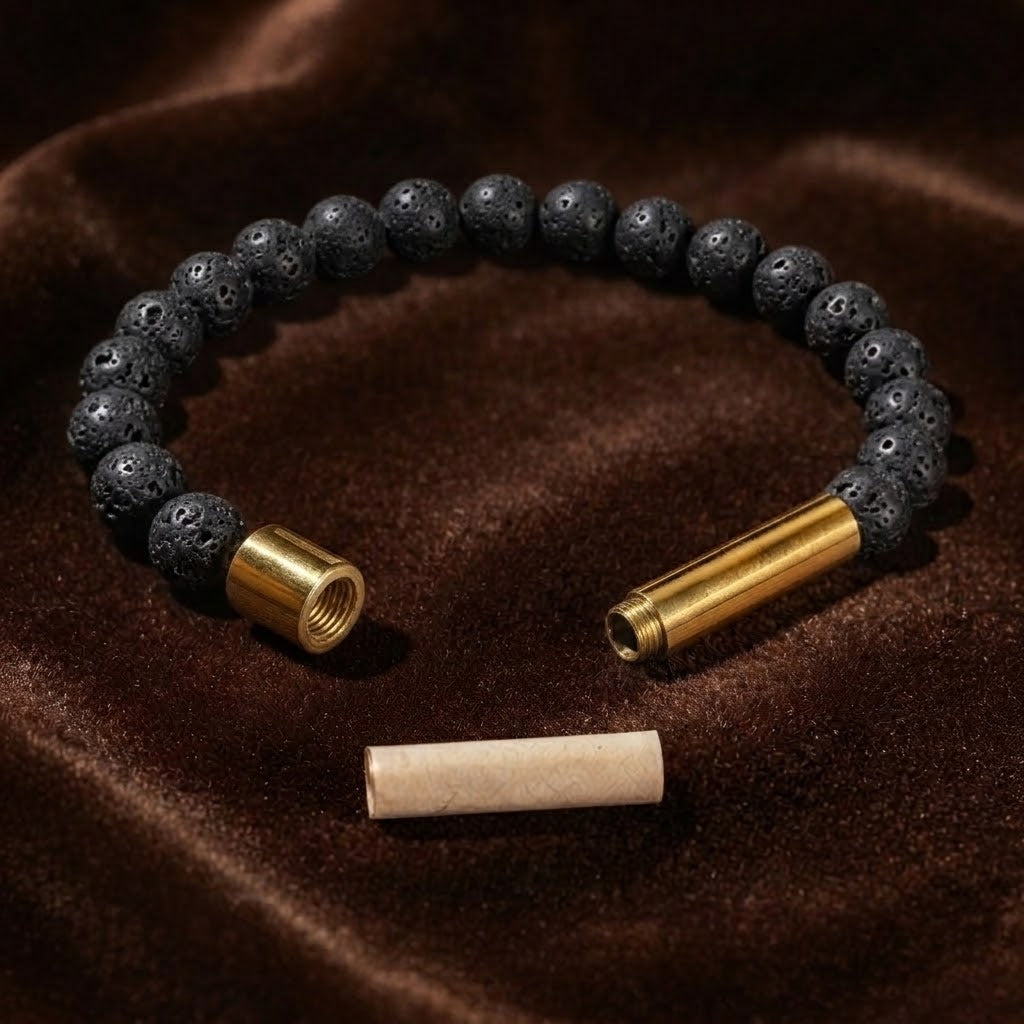 A beaded bracelet made of dark textured black beads with two gold-toned metal ends, displayed on a brown velvet surface with a small beige cylindrical piece placed below.